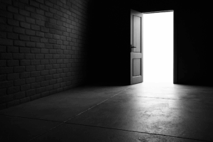 Black-and-white photograph of a long, shadowed pedestrian stairwell descending between two tall concrete walls in an urban environment. A single figure walks downward into the light, creating a visual metaphor for strategic focus and directional change. Blue accent coloring is subtly applied to the railing and ambient reflections.