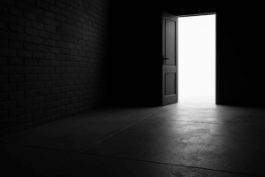 Black-and-white photograph of a long, shadowed pedestrian stairwell descending between two tall concrete walls in an urban environment. A single figure walks downward into the light, creating a visual metaphor for strategic focus and directional change. Blue accent coloring is subtly applied to the railing and ambient reflections.